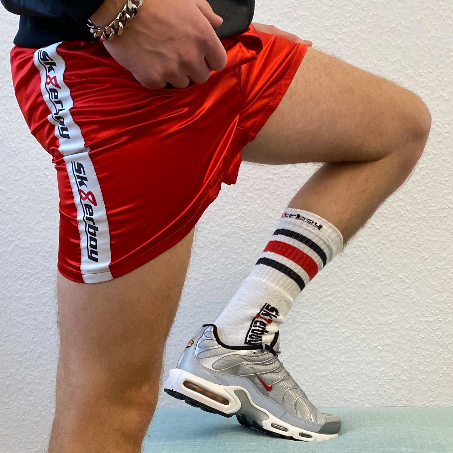 sportlicher typ mit nike tn sneaker in silver und sk8erboy tube socks zeigt seine beine und traegt eine rote boxer short in shiny red mit dicker armkette und shiny jacket