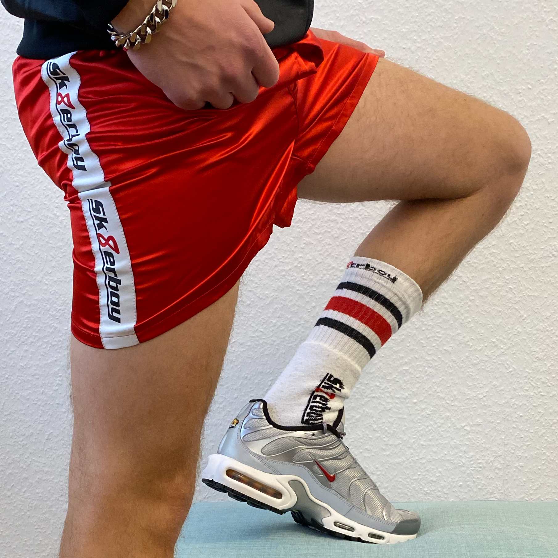 sportlicher typ mit nike tn sneaker in silver und sk8erboy tube socks zeigt seine beine und traegt eine rote boxer short in shiny red mit dicker armkette und shiny jacket
