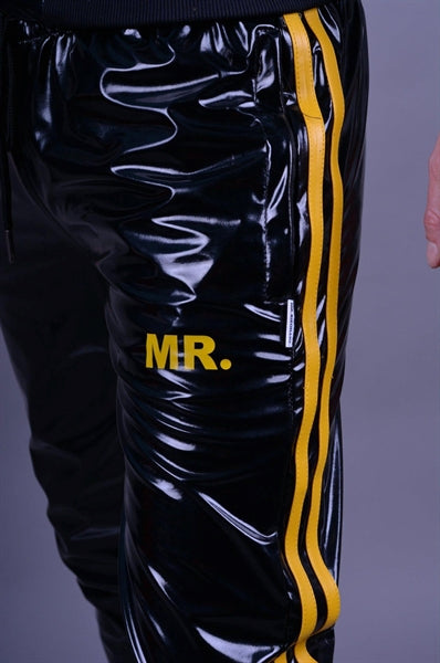 MR Riegillio PVC Tracksuit Hose mit gelben streifen von einem jungen gay getragen in schwarz glänzend mit weissen nike tn sneakern von vorne in nahaufnahme