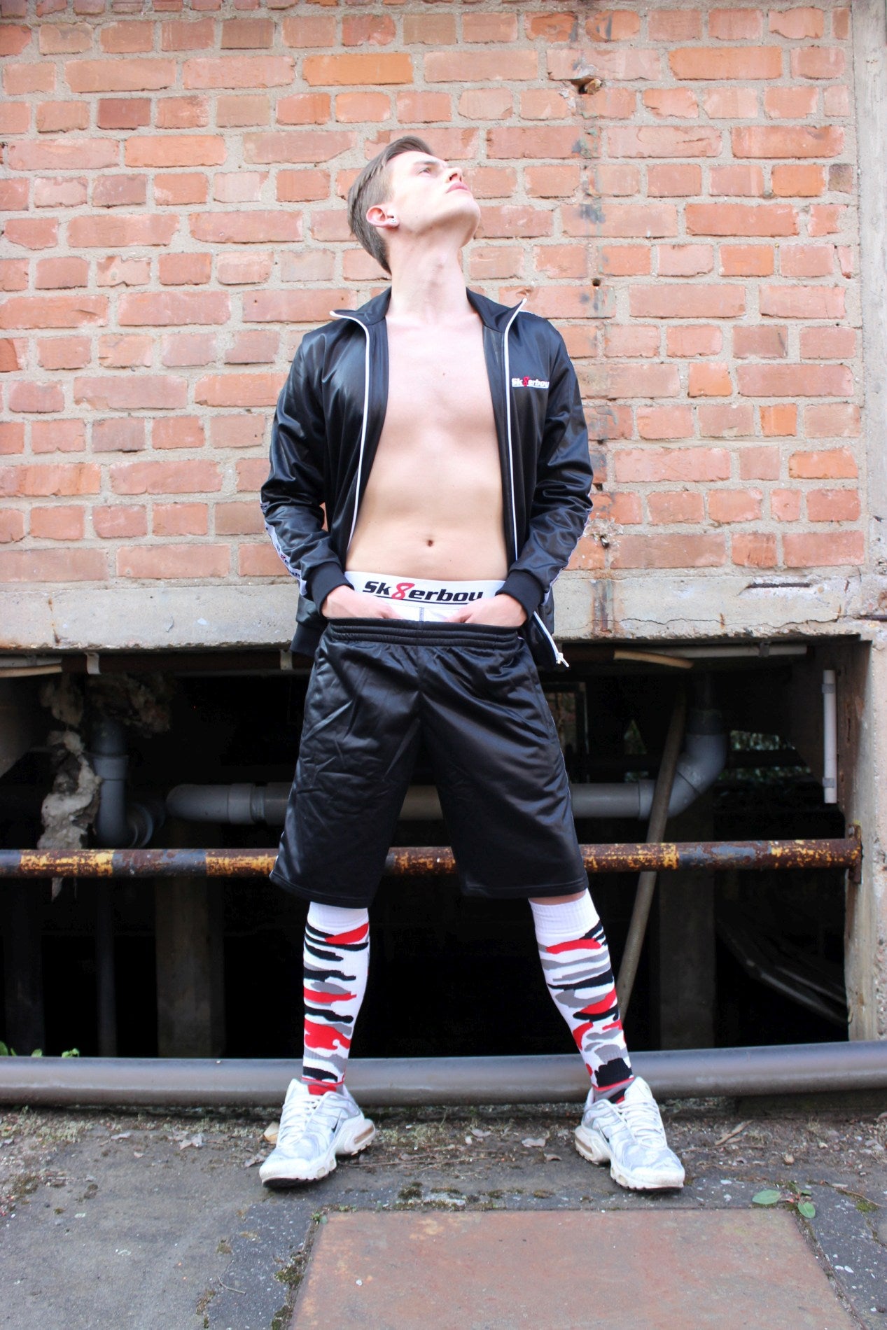 sexy gay mit freiem oberkoerper traegt einen glanz trainingsanzug von sk8erboy und passende short mit mx socks in flecktarn und nike tn sneaker